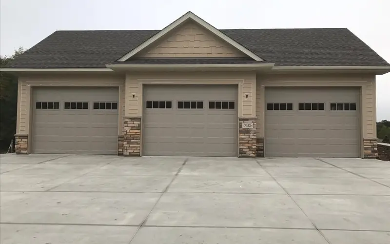Three light-colored paneled garage doors with top windows