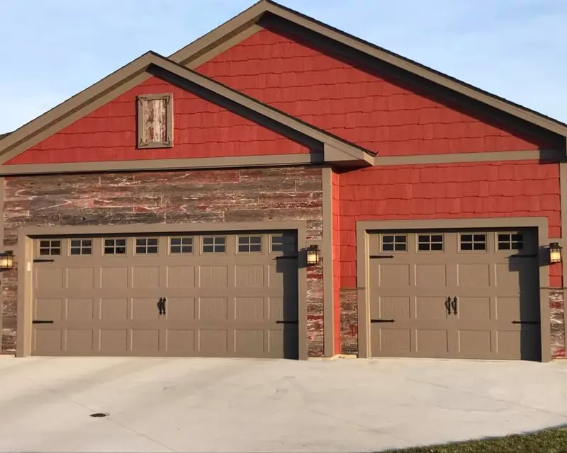 Matching double and single paneled garage doors with top windows against red siding and stone