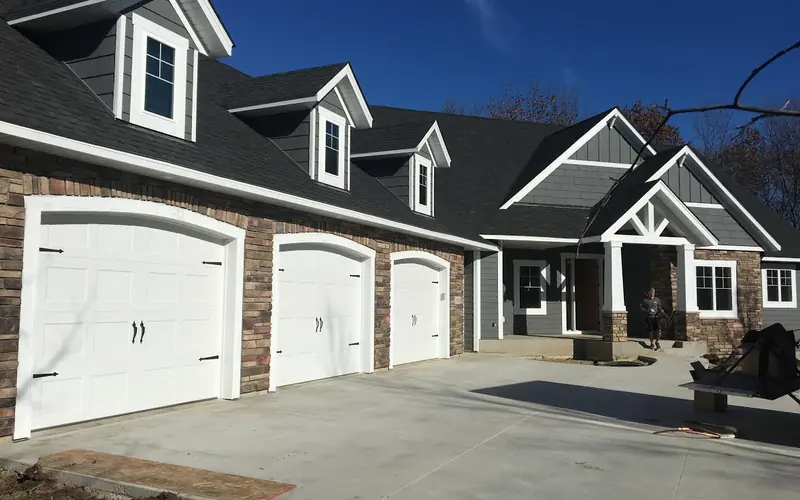 Three white paneled garage doors with decorative handles and hinges on a gray and stone home