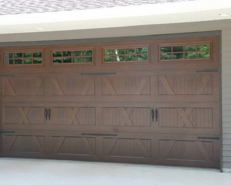 Wood-tone garage door with crossbuck panels, upper windows, and decorative hardware